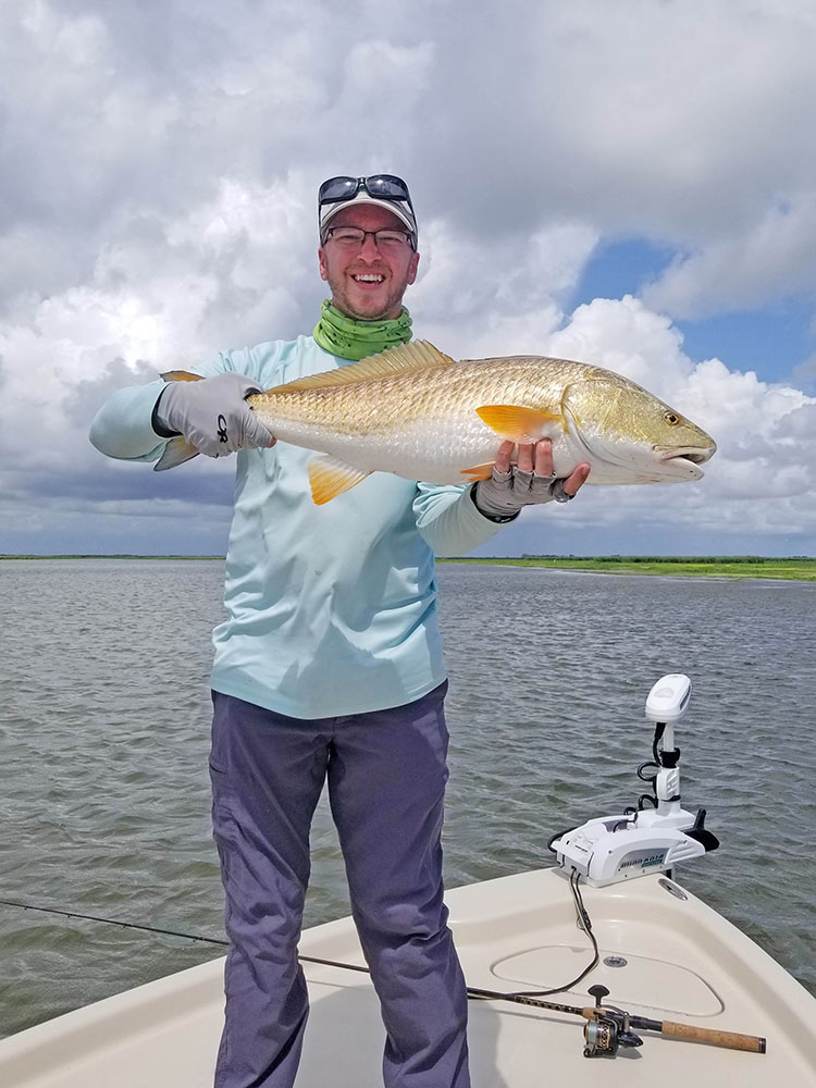 Person standing on a boat is holding up a large fish with both hands