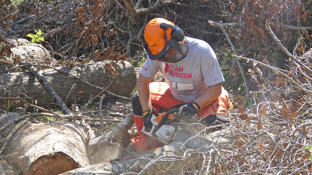 A Greyshirt cuts a large log with a chainsaw.