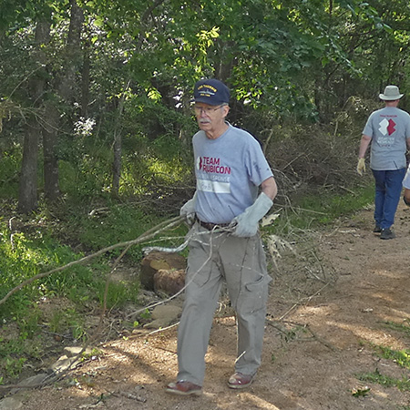 A person carrying tree branches walking on a crushed granite trail