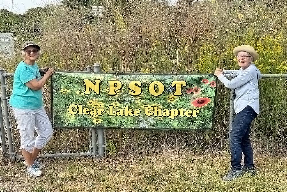 Helle and Nancy hang a banner at the entrance to the NOA I gardens.