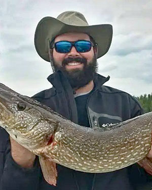 Richard is holding a large fish. He is wearing a hat and sunglasses and smiling at the camera.