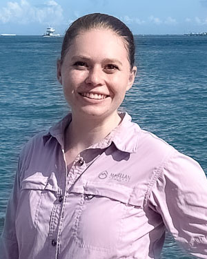 Melanie is standing in front of a large body of water on a sunny day.