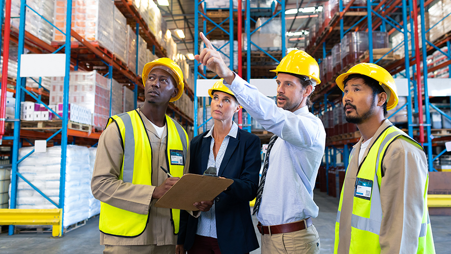 A group of people inside a warehouse receiving direction from a supervisor